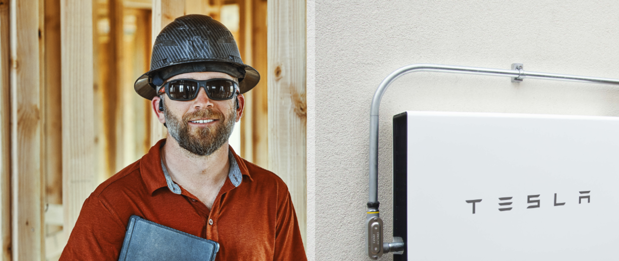 Man wearing hardhat standing next to Tesla