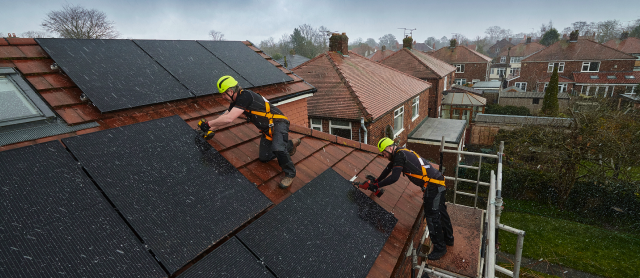 two construction workers installing solar panels on a roof